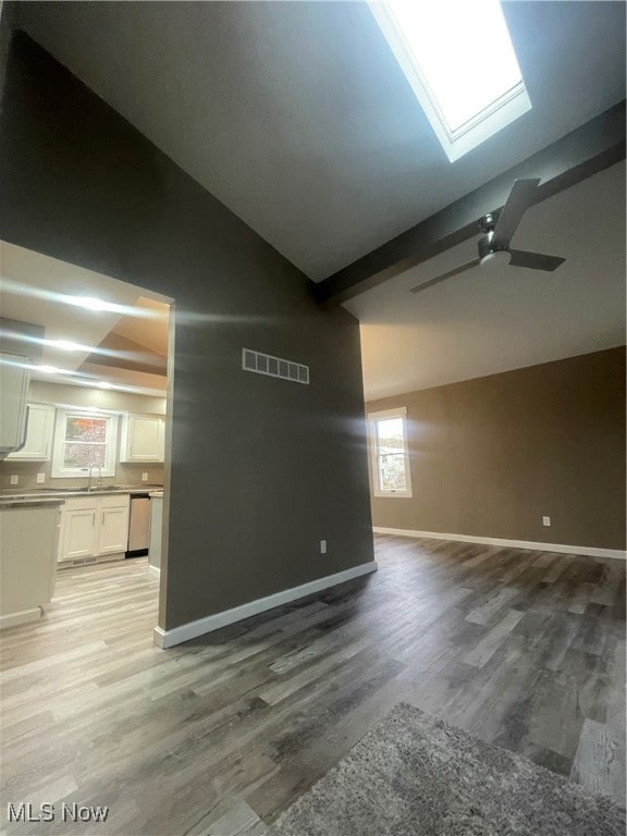 interior space featuring sink, light hardwood / wood-style flooring, beam ceiling, and a skylight