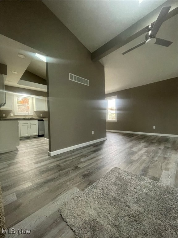 unfurnished living room featuring beam ceiling, high vaulted ceiling, sink, and hardwood / wood-style floors