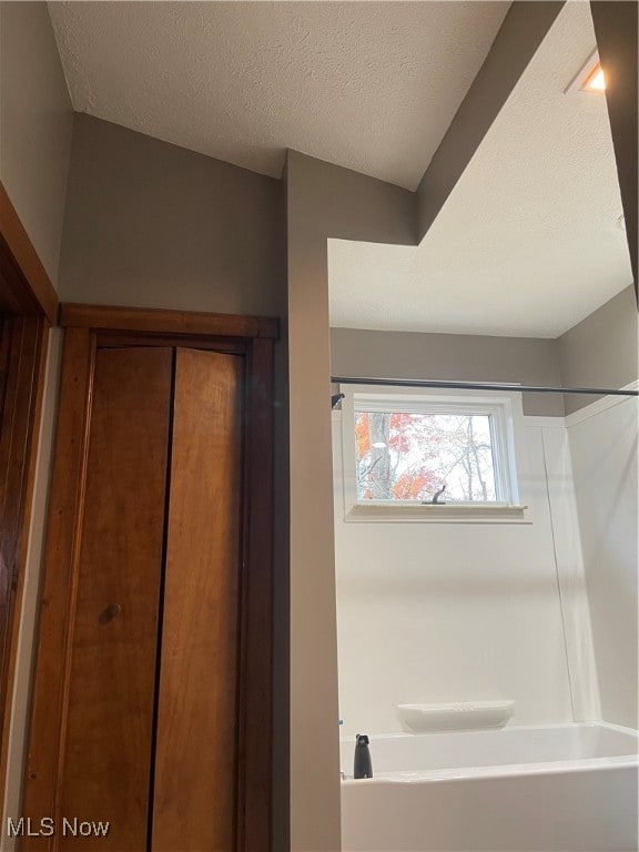 bathroom with lofted ceiling, a textured ceiling, and shower / bathing tub combination