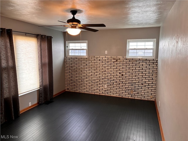 empty room featuring ceiling fan, brick wall, a textured ceiling, and dark hardwood / wood-style flooring