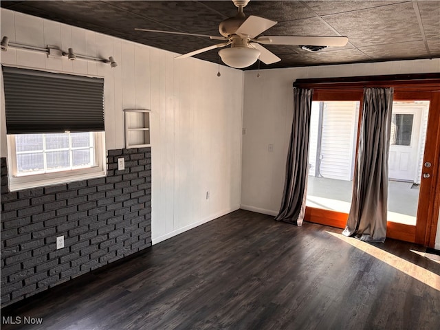 unfurnished living room featuring ceiling fan, brick wall, dark hardwood / wood-style floors, and wood walls