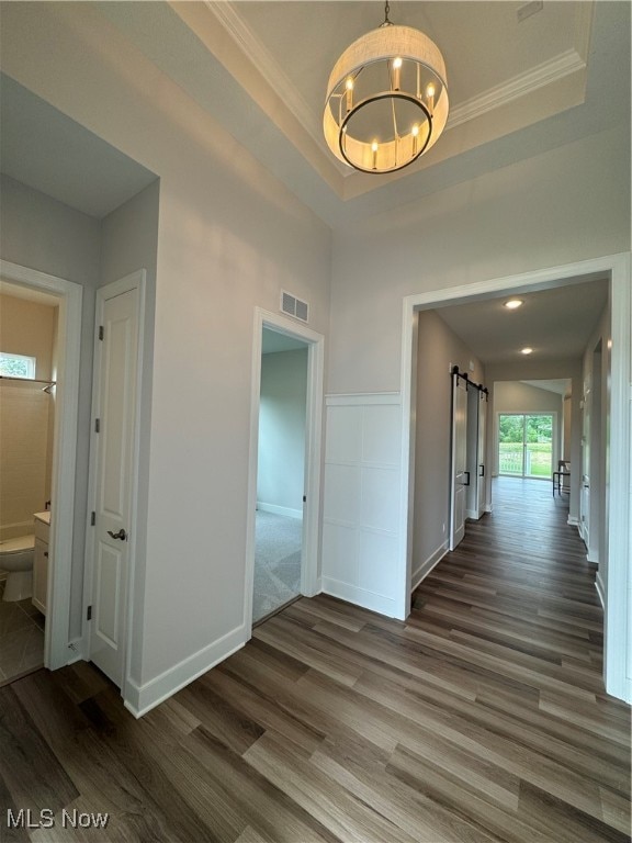 hall featuring dark hardwood / wood-style floors, a tray ceiling, ornamental molding, a barn door, and a chandelier