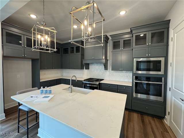 kitchen with light stone countertops, sink, dark hardwood / wood-style flooring, stainless steel appliances, and a kitchen island with sink