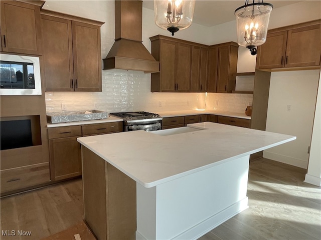 kitchen featuring a kitchen island, hanging light fixtures, stainless steel appliances, light wood-type flooring, and custom exhaust hood