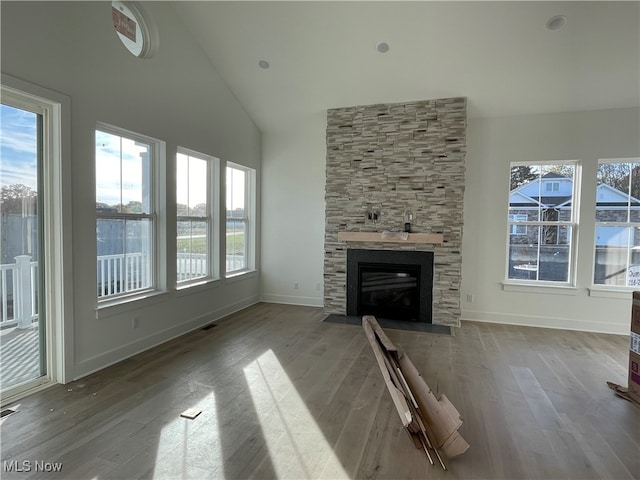 unfurnished living room featuring a stone fireplace, high vaulted ceiling, and light wood-type flooring