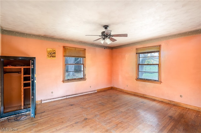 empty room featuring ceiling fan, a baseboard heating unit, and hardwood / wood-style floors