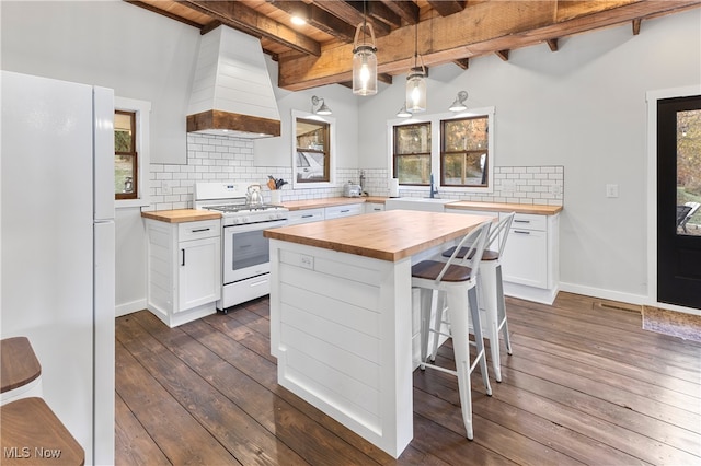 kitchen featuring white appliances, butcher block counters, hanging light fixtures, and white cabinets