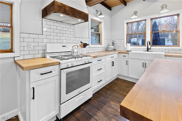 kitchen with custom range hood, gas range gas stove, white cabinetry, and wooden counters