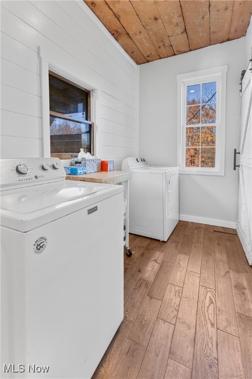 laundry room with wood ceiling, a barn door, separate washer and dryer, wood walls, and light hardwood / wood-style floors