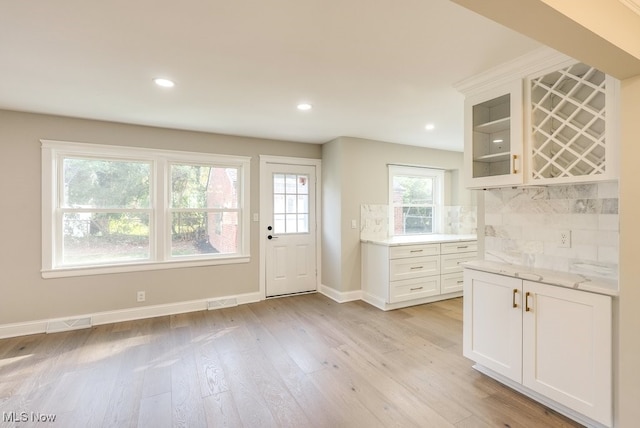 kitchen featuring white cabinetry, light stone counters, tasteful backsplash, and light hardwood / wood-style flooring