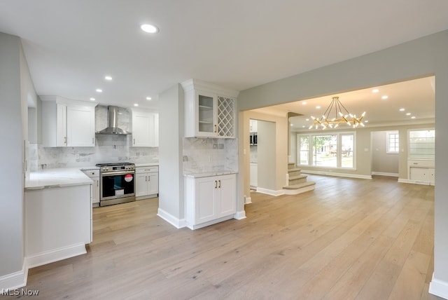 kitchen with wall chimney range hood, light hardwood / wood-style flooring, white cabinets, and stainless steel range with gas stovetop