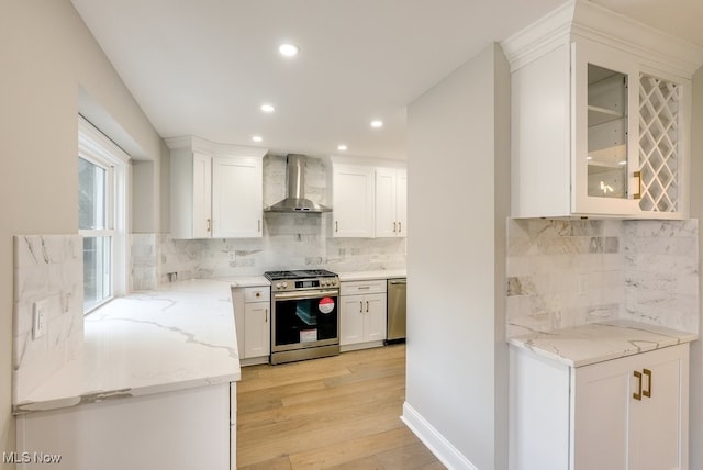 kitchen featuring appliances with stainless steel finishes, wall chimney exhaust hood, white cabinetry, and light wood-type flooring