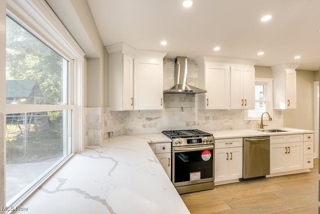 kitchen with wall chimney exhaust hood, sink, white cabinets, light wood-type flooring, and appliances with stainless steel finishes