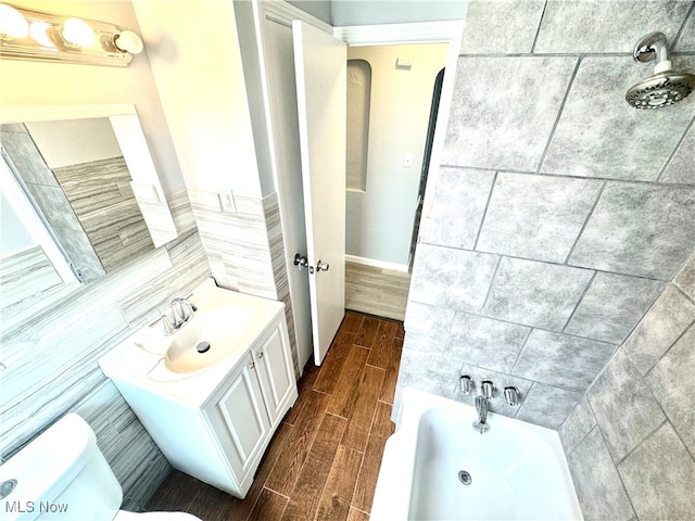 bathroom with toilet, a tub to relax in, vanity, hardwood / wood-style floors, and tile walls