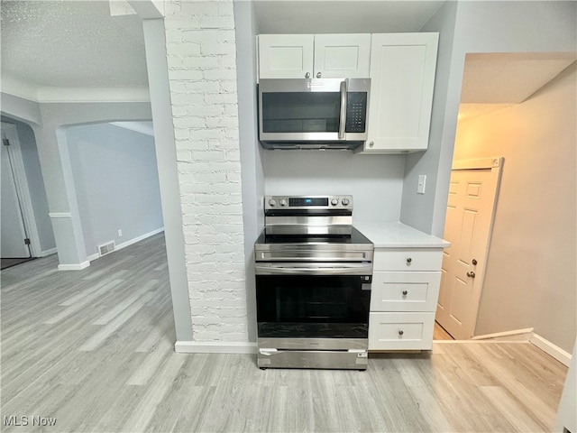 kitchen with appliances with stainless steel finishes, light hardwood / wood-style flooring, white cabinetry, and a textured ceiling