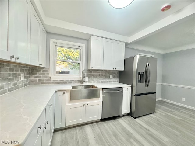 kitchen with light hardwood / wood-style flooring, stainless steel appliances, backsplash, sink, and white cabinetry