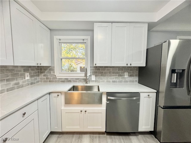 kitchen with appliances with stainless steel finishes, light hardwood / wood-style flooring, white cabinetry, and tasteful backsplash