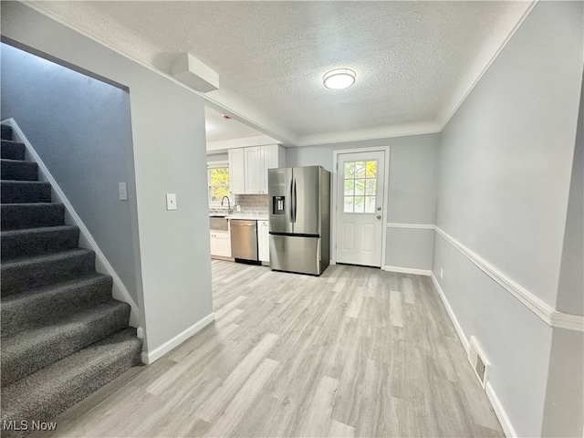 kitchen featuring backsplash, appliances with stainless steel finishes, white cabinetry, a textured ceiling, and light hardwood / wood-style flooring