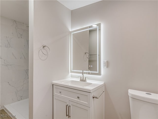 bathroom featuring vanity, a tile shower, and toilet