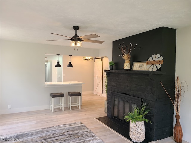 living room featuring light hardwood / wood-style floors, a barn door, a fireplace, and ceiling fan