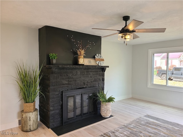 living room featuring light hardwood / wood-style floors, a stone fireplace, a textured ceiling, and ceiling fan