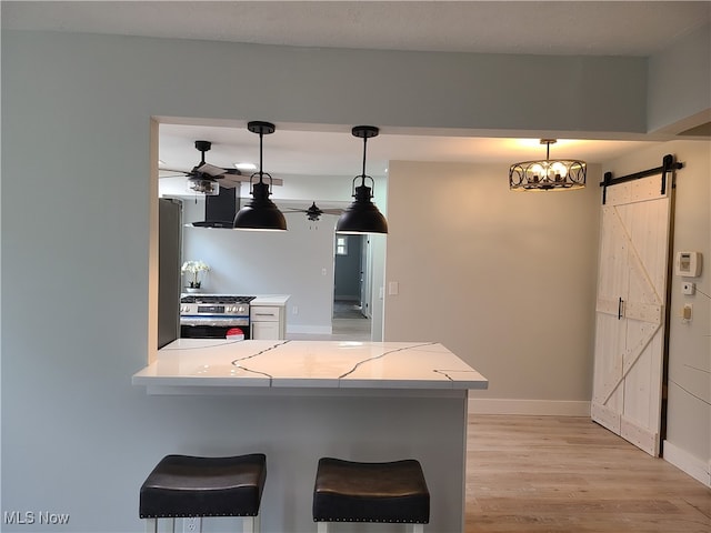 kitchen with a kitchen bar, a barn door, kitchen peninsula, hanging light fixtures, and stainless steel gas range oven