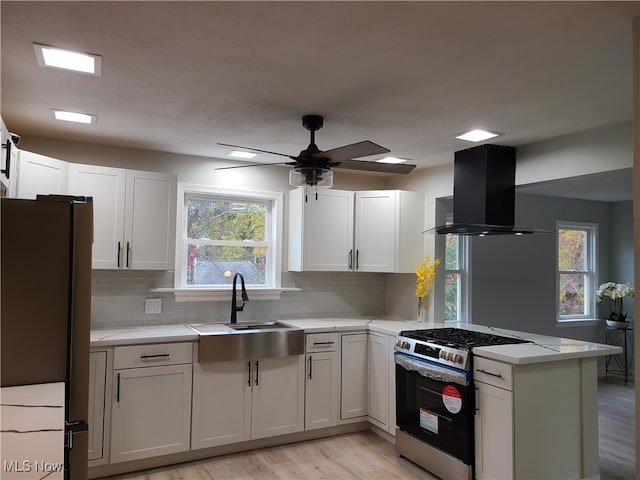 kitchen featuring fridge, gas range oven, kitchen peninsula, white cabinetry, and ventilation hood