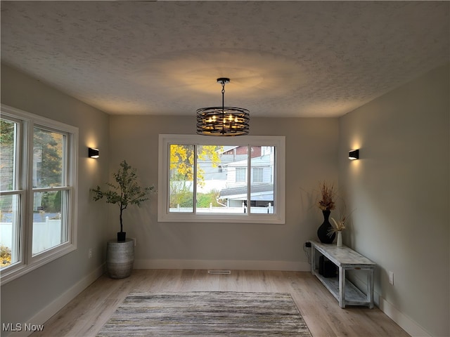 unfurnished dining area with light hardwood / wood-style flooring, a textured ceiling, and a notable chandelier