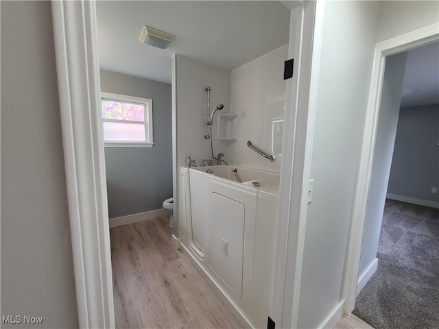 bathroom with toilet, a washtub, and hardwood / wood-style floors