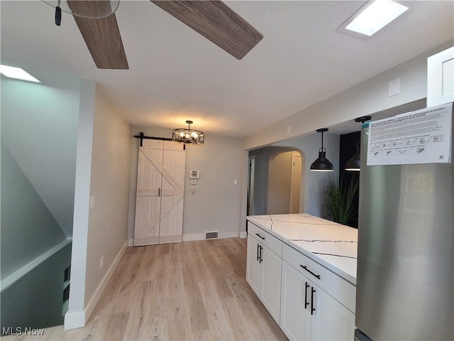 kitchen with a barn door, pendant lighting, light wood-type flooring, white cabinets, and stainless steel refrigerator