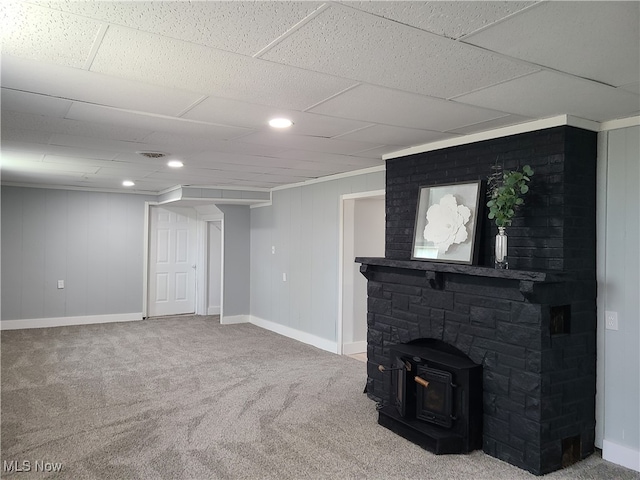 unfurnished living room with carpet, a paneled ceiling, and a wood stove