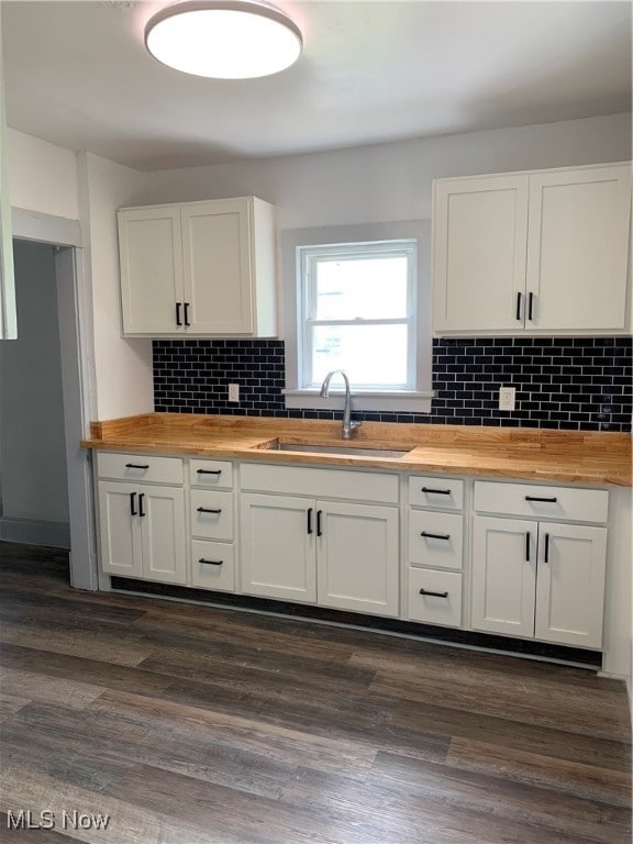 kitchen featuring sink, butcher block countertops, backsplash, dark hardwood / wood-style flooring, and white cabinets