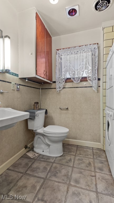 bathroom featuring tile walls, sink, stacked washer / drying machine, and toilet