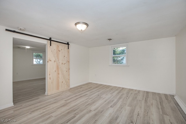 unfurnished room with plenty of natural light, light wood-type flooring, and a barn door