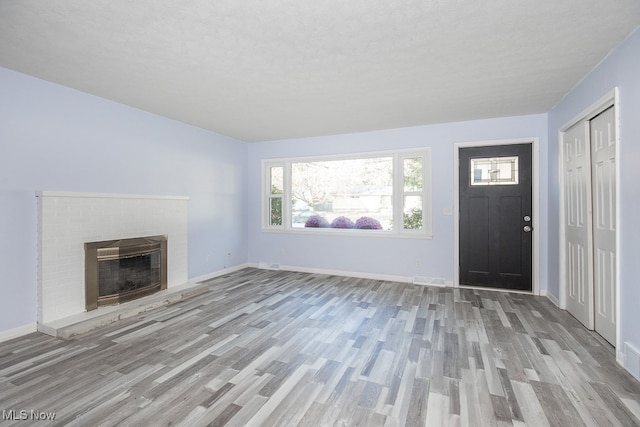 unfurnished living room with light hardwood / wood-style flooring, a brick fireplace, and a textured ceiling