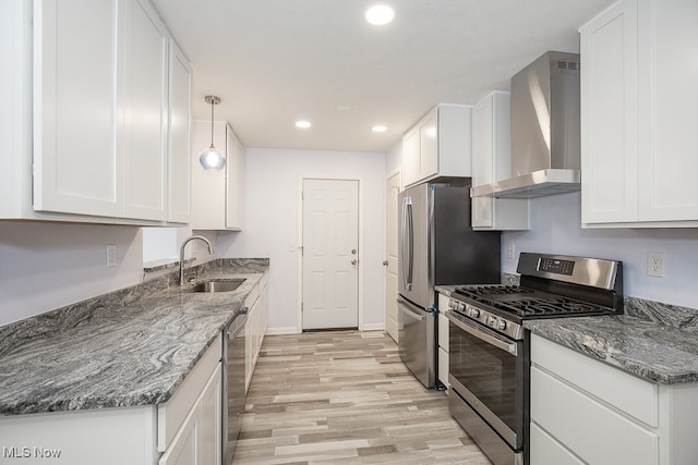 kitchen with wall chimney range hood, appliances with stainless steel finishes, white cabinetry, light hardwood / wood-style floors, and sink