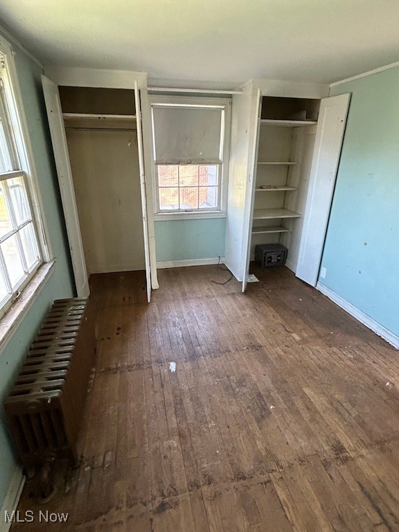 unfurnished bedroom with dark wood-type flooring, radiator, and multiple closets