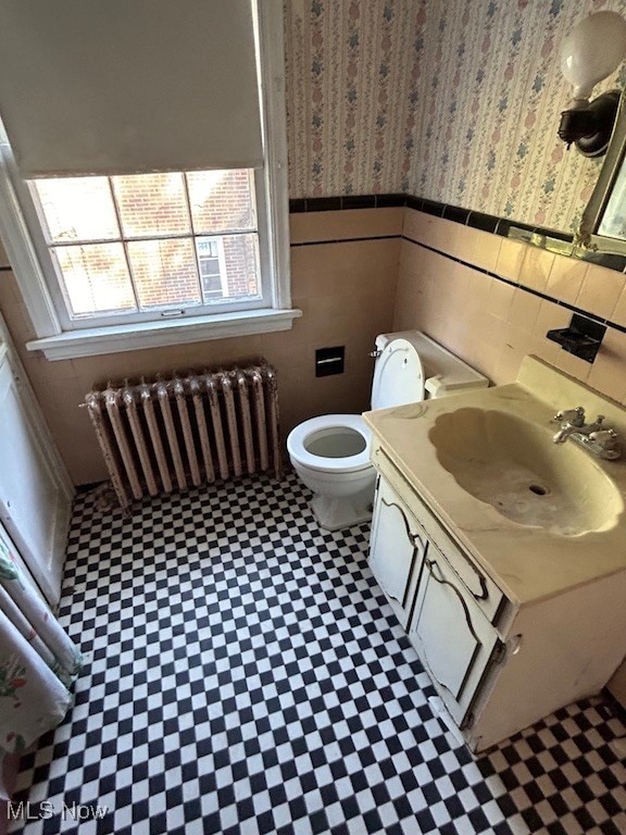 bathroom with tile walls, vanity, toilet, and radiator