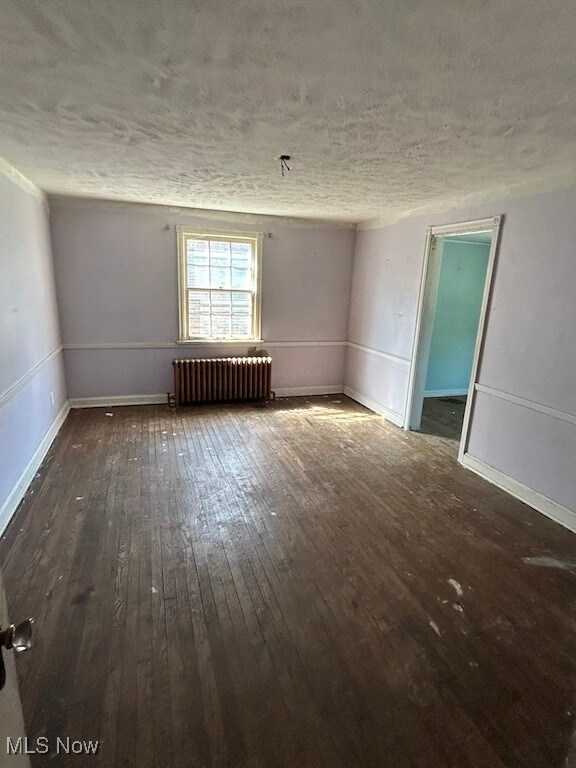 empty room with radiator heating unit, dark wood-type flooring, and a textured ceiling