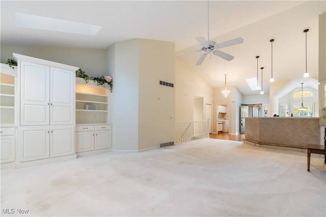 unfurnished living room featuring ceiling fan with notable chandelier, light colored carpet, high vaulted ceiling, and a skylight