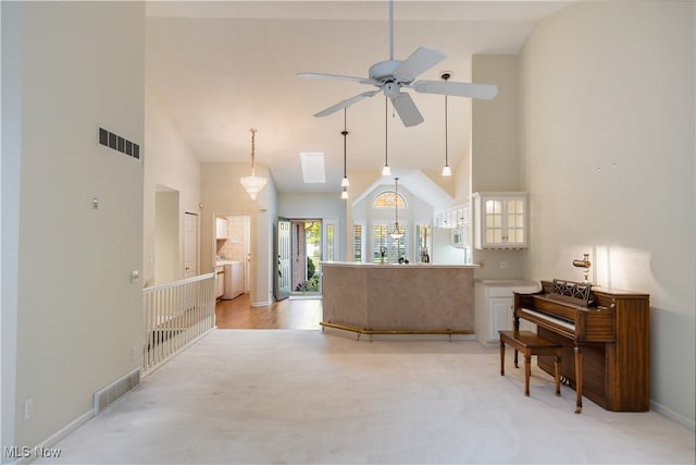 carpeted living room with high vaulted ceiling, ceiling fan with notable chandelier, and a skylight