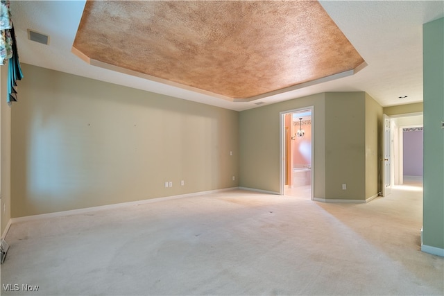 carpeted empty room with a textured ceiling and a raised ceiling