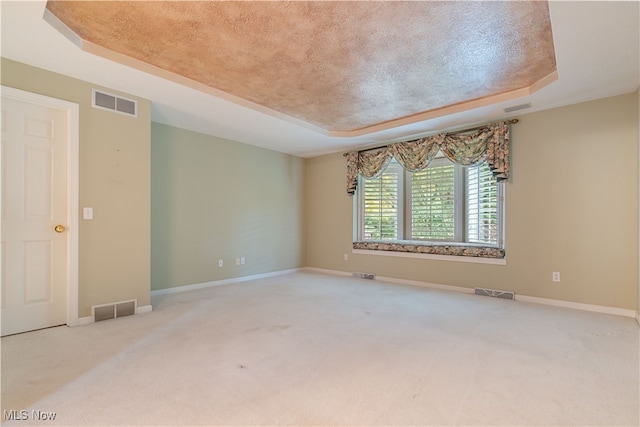 spare room with a textured ceiling, a tray ceiling, and carpet floors