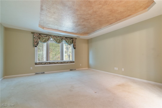 carpeted spare room with a textured ceiling and a tray ceiling