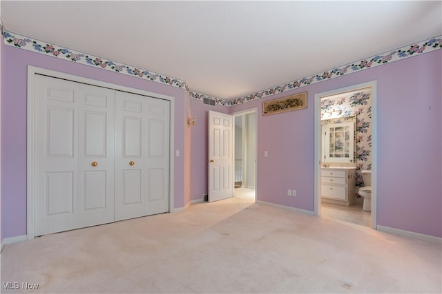 unfurnished bedroom featuring light carpet, ensuite bathroom, and a closet