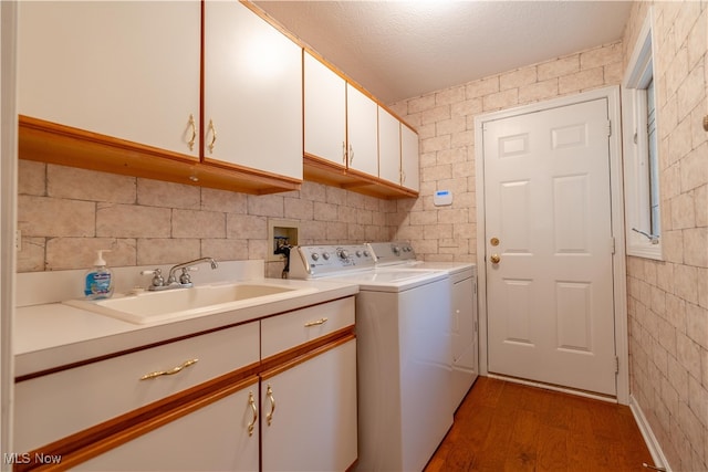 laundry area with cabinets, a textured ceiling, washing machine and clothes dryer, dark wood-type flooring, and sink