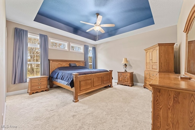 bedroom with a tray ceiling, multiple windows, ceiling fan, and light colored carpet