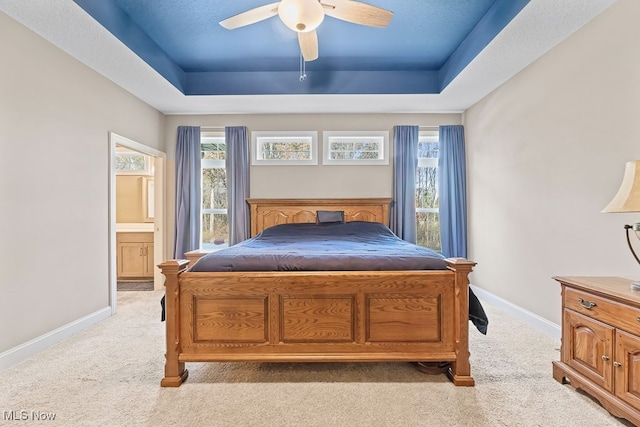 carpeted bedroom with ensuite bathroom, ceiling fan, and a raised ceiling