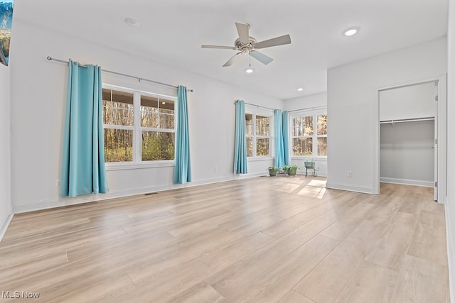 interior space featuring ceiling fan, a walk in closet, light hardwood / wood-style flooring, and multiple windows