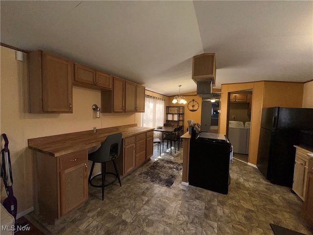 kitchen featuring butcher block counters, black fridge, a chandelier, washing machine and dryer, and pendant lighting